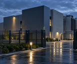 Synthetic editorial illustration. Unbranded data-centre exterior with cooling infrastructure and secure perimeter for cybersecurity news.