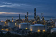 Synthetic editorial illustration. Unbranded refinery storage tanks and distillation columns at blue-hour dawn for energy-market news.
