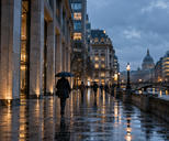 Synthetic editorial illustration. Rain-washed European financial district at blue hour with distant pedestrians and illuminated office buildings.