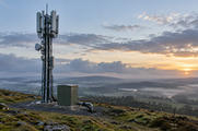 Synthetic editorial illustration. Unbranded cellular relay mast above a misty rural landscape for telecom and connectivity news.