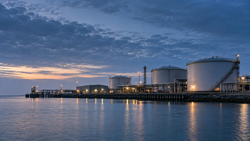 Synthetic editorial illustration. Unbranded waterfront energy terminal with storage tanks and pipework for energy-market news.