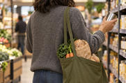 Synthetic editorial illustration. Anonymous shopper choosing an unbranded tin beside a reusable bag of staple groceries for consumer-inflation news.