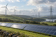 Synthetic editorial illustration. Wind turbines, solar panels and transmission infrastructure across a green landscape for climate-finance and renewable-energy news.