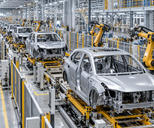 Synthetic editorial illustration. Unbranded electric vehicle bodies and robotic arms on a modern automotive assembly line.