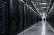 Synthetic editorial illustration. Unbranded high-density server racks and distant technician in an operational data-centre aisle.