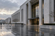 Synthetic editorial illustration. Unbranded institutional financial building with rain-washed paving for central-bank and interest-rate news.
