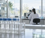 Synthetic editorial illustration. Anonymous researcher working with an unbranded optical instrument in a bright biotech laboratory.