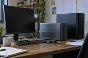 Synthetic editorial illustration. Generic small desktop computer and taller computing tower in an engineering office, with an entirely off monitor; local workstation hardware, not a real named product.