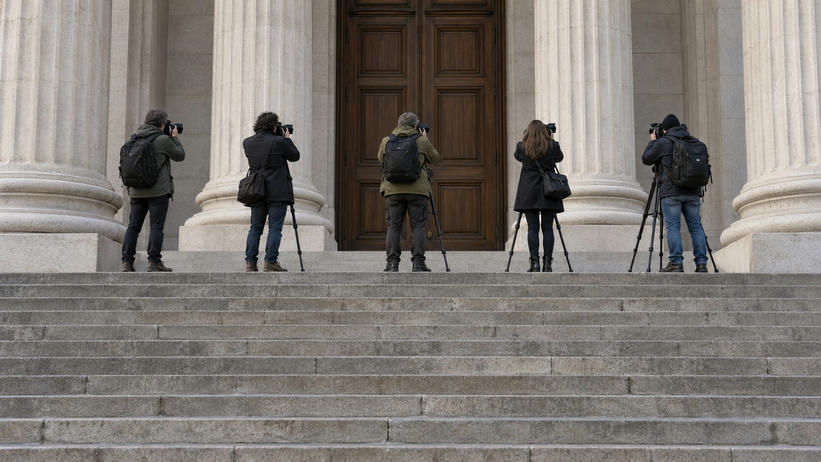 Synthetic editorial illustration. Broad courthouse steps lead to tall stone columns and closed wooden doors. Five rear-facing photographers wait on the upper landing with cameras, tripods and shoulder bags.