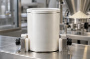 Synthetic editorial illustration. A single plain cylindrical powder tin in a food-factory inspection cradle, with stainless powder-handling equipment blurred behind it.