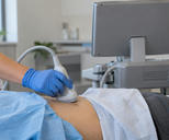 Synthetic editorial illustration. A blue-gloved hand holds an ultrasound probe against a draped patient's abdomen. The plain back of the monitor faces the camera beside unlabeled clinical supplies; no heads are visible.