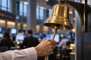 Synthetic editorial illustration. A business-shirted adult hand pulls the hanging clapper cord of a mounted brass bell, with a softly defocused occupied business floor behind it.