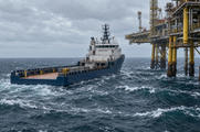 Synthetic editorial illustration. An offshore work site. A blue supply vessel with an open aft deck sits alongside a steel platform above choppy waves and whitecaps under an overcast sky.