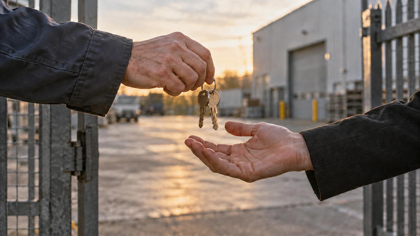 Synthetic editorial illustration. Two cropped adults exchange a small key ring at a plain industrial-property entrance.