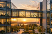 Synthetic editorial illustration. A corporate office campus. A glazed skybridge connects two modern buildings above landscaped paths, with two small silhouettes crossing inside as golden sunlight shines between the facades.