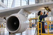Synthetic editorial illustration. A technician on a platform inspects an outboard wing hatch; the fuselage, wing root and engine suspended below the wing by a pylon are visible as separate structures.