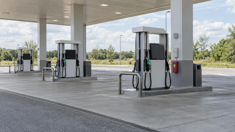Synthetic editorial illustration. Generic unbranded motor-fuel dispensers and forecourt under a roadside filling-station canopy, with blank/off displays; fuel retail, not natural-gas processing or EV charging.