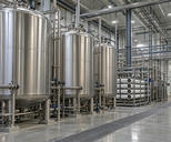 Synthetic editorial illustration. An industrial water-treatment hall. Tall stainless tanks, filtration housings and dense polished pipework line a clean utility space with floor drainage grilles and overhead lighting.