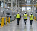 Synthetic editorial illustration. A factory production hall. Three inspectors seen from behind walk along a marked aisle carrying clipboards, wearing bright safety vests and hard hats among machinery and pipework.
