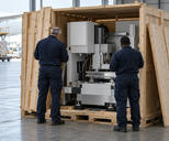 Synthetic editorial illustration. An airport cargo hall. Two officers seen from behind inspect a precision machine inside a partly opened wooden crate, with cargo pallets and an aircraft beyond the loading area.
