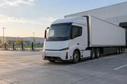 Synthetic editorial illustration. Generic unbranded electric cargo tractor and plain trailer at an anonymous freight depot beside ordinary charging infrastructure.