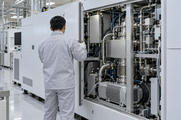 Synthetic editorial illustration. A semiconductor equipment service area. An engineer seen from behind holds open a machine side panel, revealing a vacuum pump, metal bellows, valves and bundled lines inside the enclosure.
