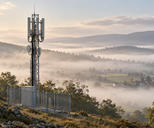 Synthetic editorial illustration. A cellular relay mast and its base cabinet stand above a misty rural valley.