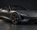 Synthetic editorial illustration. A matte graphite open-top sports car stands alone in a dark studio. Soft rim lighting outlines its low body, plain wheels and narrow headlamps against the quiet background.