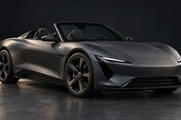 Synthetic editorial illustration. A matte graphite open-top sports car stands alone in a dark studio. Soft rim lighting outlines its low body, plain wheels and narrow headlamps against the quiet background.