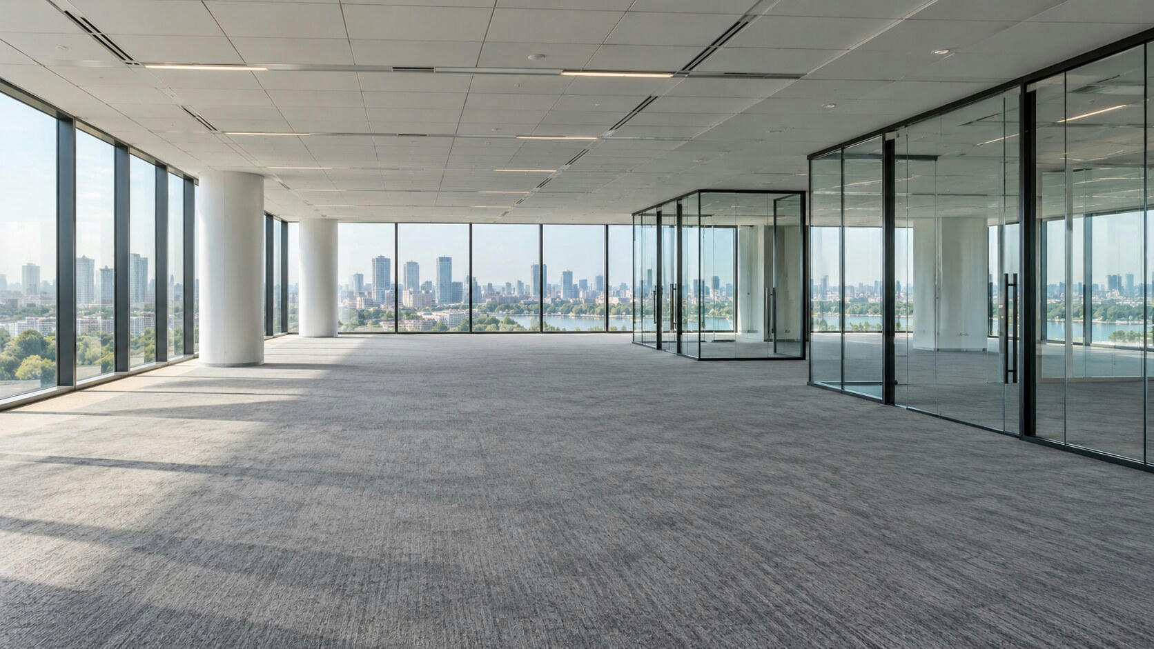 Synthetic editorial illustration. An empty office floor. Bare grey carpet stretches between white columns and glass-walled rooms, with daylight casting long window shadows and a distant city visible beyond the glazing.