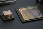Synthetic editorial illustration. A small stack of thin reflective silicon layers sits on a dark package beside a larger patterned processor die. Both rest on a textured black anti-static mat under soft inspection light.