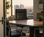 Synthetic editorial illustration. One empty practical executive chair as the focal subject at a modest meeting table, viewed through an office doorway.