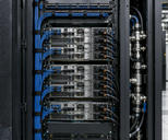 Synthetic editorial illustration. The open mesh door of a cabinet frames installed rack servers, organised network leads and connected power cables. A vertical metal pipe assembly sits beside the rack, with more cabinets receding along the aisle.
