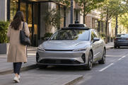 Synthetic editorial illustration. Generic unbranded electric passenger car with modest rooftop sensing equipment at an anonymous urban pickup bay; no real named vehicle, company or incident.