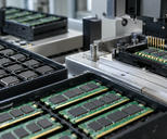 Synthetic editorial illustration. Generic packaged integrated circuits and memory boards in anti-static trays beside an electrical test fixture. Chip assembly/packaging and testing, not wafer fabrication or laptop assembly. No actual named company, product, site, person or event is depicted.