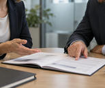 Synthetic editorial illustration. Two cropped adults discuss one populated dossier across a small round meeting table.