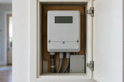 Synthetic editorial illustration. One plain household electrical meter with an off blank display and enclosed service connections, in an open domestic utility cabinet.