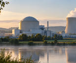 Synthetic editorial illustration. A generic domed power-station building and cooling tower are framed across a river at dawn.