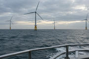 Synthetic editorial illustration. Generic utility wind turbines operating in open water, viewed from a service-vessel railing. Offshore wind electricity production, not oil or gas extraction. No actual named company, product, site, person or event is depicted.