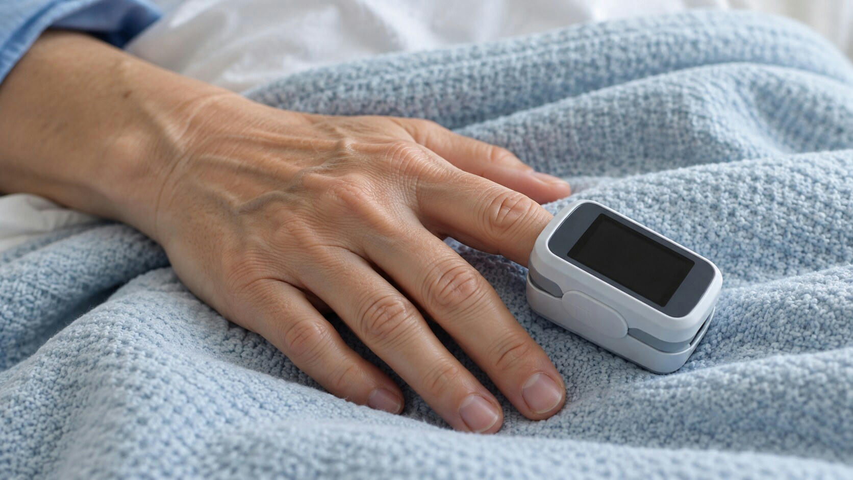 Synthetic editorial illustration. A plain white-and-grey clip device with a completely dark display sits on a patient's finger. The hand rests on a pale blue textured hospital blanket in soft clinical light.
