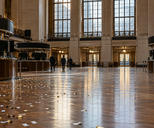 Synthetic editorial illustration. An exchange hall contains curved trading desks and dark display panels. Small paper confetti pieces lie across the polished floor as three distant rear-facing people walk toward the doors.