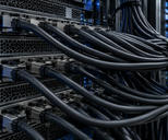 Synthetic editorial illustration. A server rack. Dense bundles of smooth dark network cables connect to metal ports across stacked equipment trays, with small blue status lights beside perforated ventilation panels.