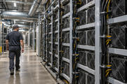 Synthetic editorial illustration. A credible unbranded digital-asset compute facility with compact processor enclosures, organized power cabling and simple cooling ducts, quiet observational industrial view, no coins or cryptocurrency logos.