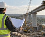 Synthetic editorial illustration. A civil engineer seen from behind reviewing an unmarked rolled plan at the edge of a working bridge construction site, credible concrete piers and construction equipment in the distance.