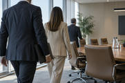 Synthetic editorial illustration. A calm observational scene of anonymous executives entering a functional corporate meeting room, one person holding a closed plain folder, no identifiable faces, no staged handshake or ceremonial pose.
