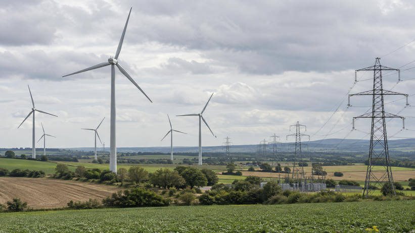 Synthetic editorial illustration. A natural documentary landscape showing a working onshore wind farm and electricity transmission connections amid agricultural fields, plausible turbine scale and soft overcast light, no symbolic eco props.