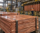 Synthetic editorial illustration. A copper processing facility with realistic thick copper cathode plates stacked in bundles and machinery deeper in the building, natural industrial light and tactile metal surfaces.