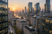 Synthetic editorial illustration. An elevated documentary view of a generic international financial district at dawn with several architectural styles, commuters small at street level, neutral glass buildings and no recognizable landmark.